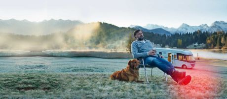 Ein mann sitzt mit seinem Hund auf einem Stuhl - im Hintergrund ein Wohnmobil