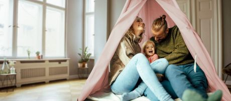 Eltern sitzen mit Tochter in einem rosa Zelt im Wohnzimmer