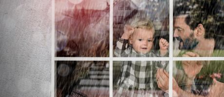 Mann und Kind schauen bei Regen durch ein Fenster