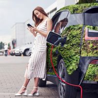 Frau steht an ihrem ladenen E-Auto, das mit Gras beklebt ist